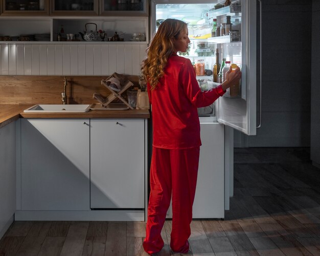 Mujer de tiro completo revisando el refrigerador por la noche