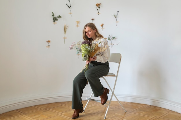 Mujer de tiro completo sentada en una silla con flores