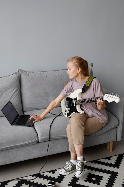 Mujer de tiro completo en el sofá con la guitarra