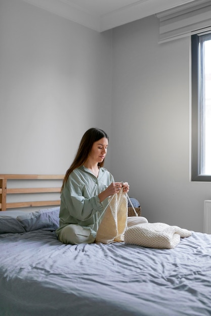 Mujer de tiro completo tejiendo en la cama