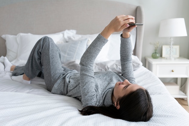 Mujer de tiro completo con teléfono inteligente en la cama