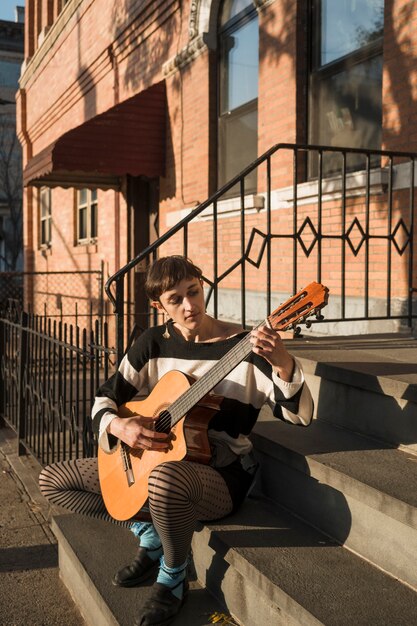 Mujer de tiro completo tocando la guitarra en las escaleras