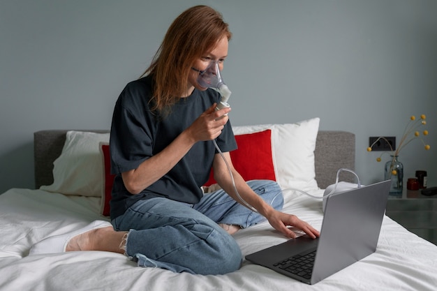 Mujer de tiro completo usando nebulizador en casa