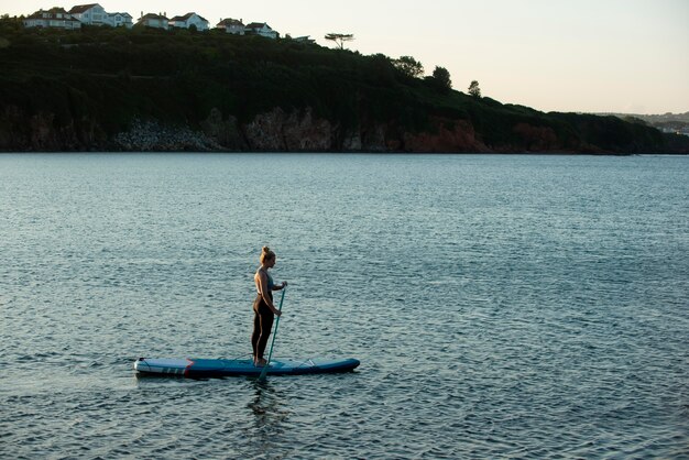 Mujer de tiro largo paddleboarding