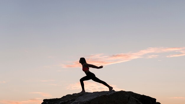 Mujer de tiro largo de pie en una posición deportiva sobre una roca con espacio de copia