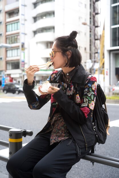 Mujer de tiro medio comiendo comida callejera japonesa al aire libre