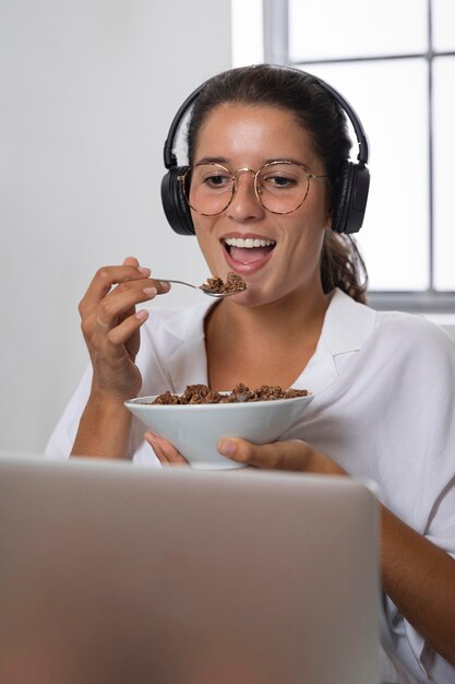 Mujer de tiro medio comiendo delante de la computadora portátil