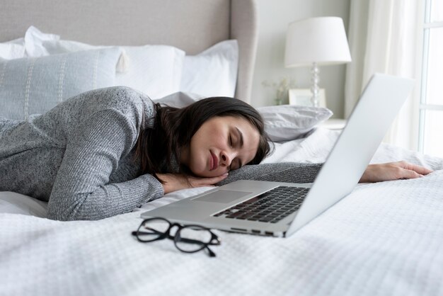 Mujer de tiro medio durmiendo cerca de la computadora portátil