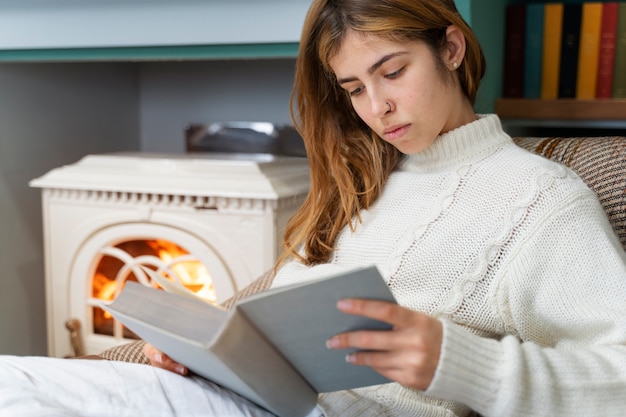 Foto gratuita mujer de tiro medio leyendo junto a la chimenea