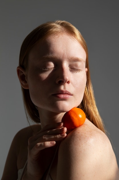 Mujer de tiro medio posando con mandarina