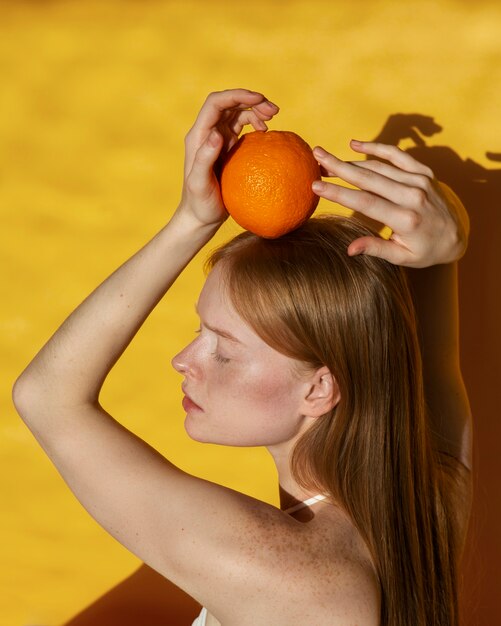 Mujer de tiro medio posando con naranja.