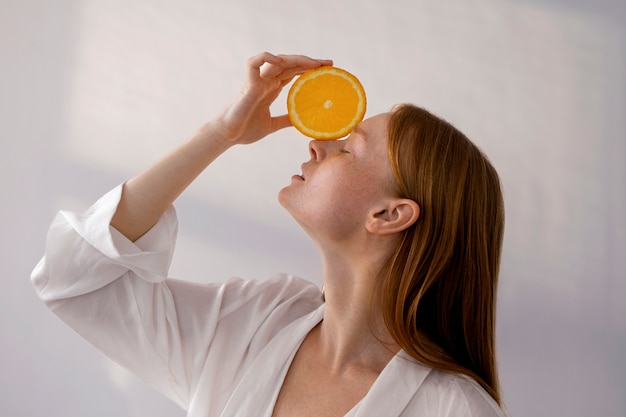 Mujer de tiro medio posando con rodaja de naranja