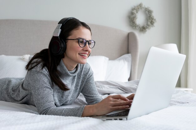 Mujer de tiro medio que trabaja con una computadora portátil en el dormitorio