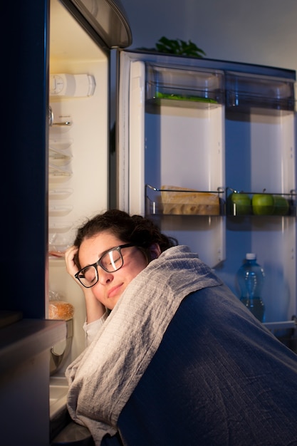 Mujer de tiro medio revisando la nevera en busca de un refrigerio