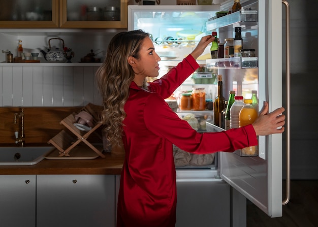 Foto gratuita mujer de tiro medio revisando el refrigerador por la noche