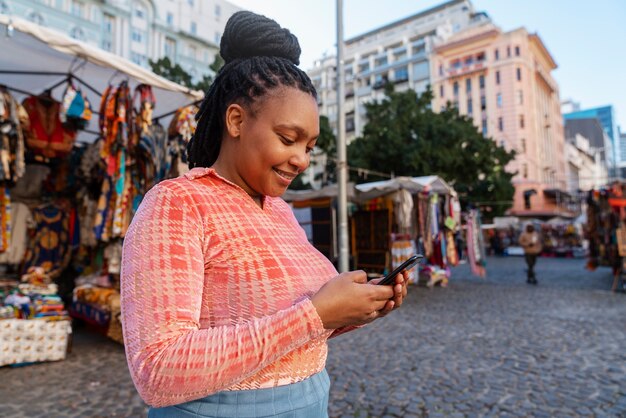 Mujer de tiro medio usando un teléfono inteligente al aire libre