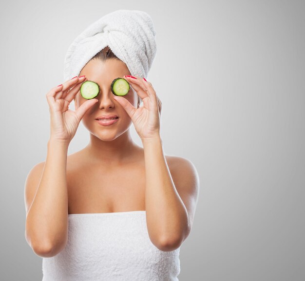 mujer en una toalla sonriendo con el pepino en los ojos