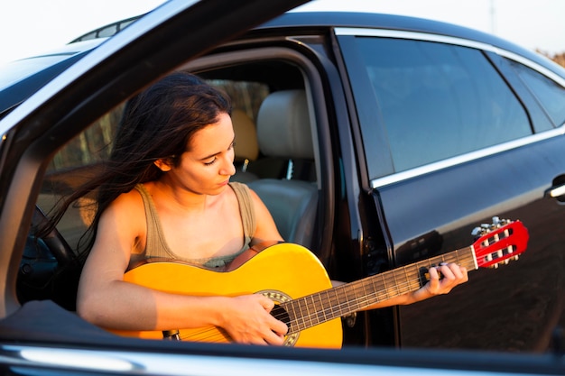 Foto gratuita mujer tocando la guitarra mientras está en el asiento de su automóvil