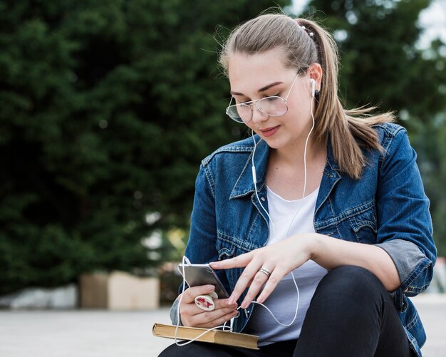 Mujer tocando la pantalla del teléfono inteligente sentado en el parque