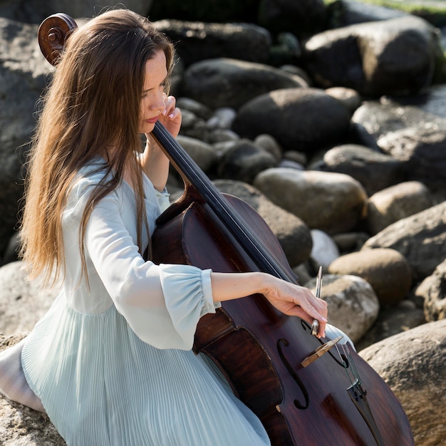 Foto gratuita mujer tocando el violonchelo junto al mar con rocas