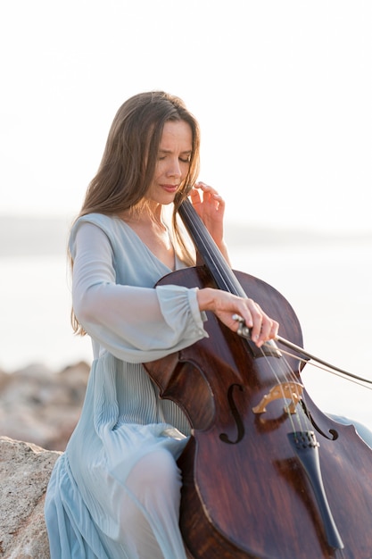 Mujer tocando el violonchelo en las rocas al aire libre