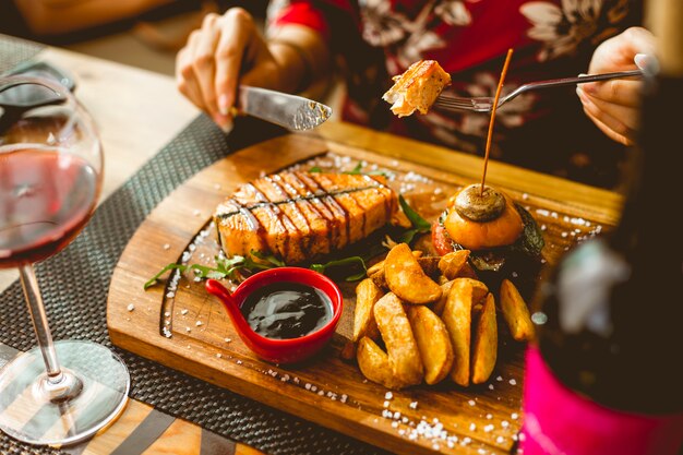 Mujer toma salmón a la parrilla con patata casera berenjena pimiento champiñón tomate vista lateral