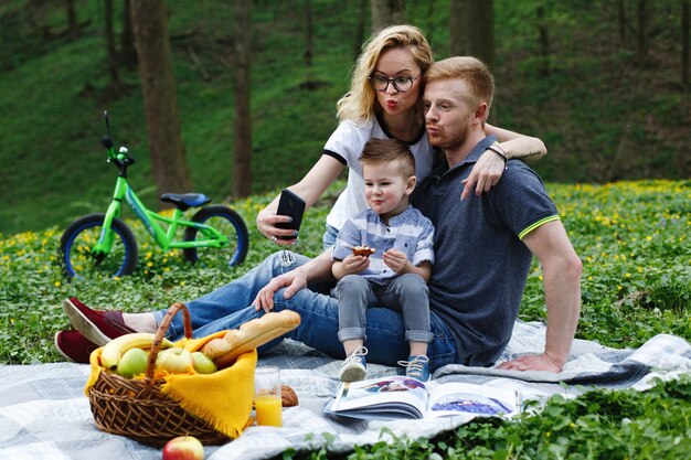 La mujer toma un selfie con sus padres y su hijo sentado en un plaid en el parque