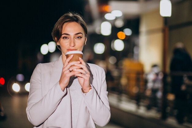 Mujer tomando café afuera en la calle por la noche