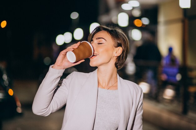 Mujer tomando café afuera en la calle por la noche