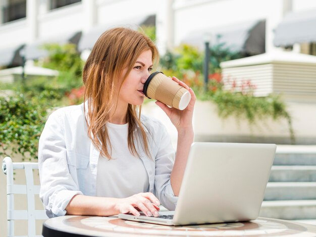 Mujer tomando café al aire libre mientras trabajaba en la computadora portátil