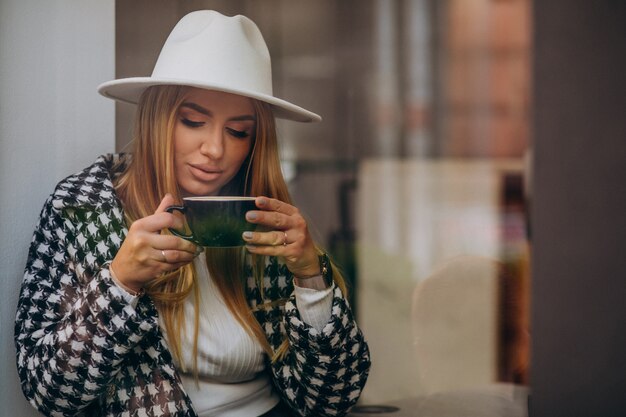 Mujer tomando café en un café, sentado detrás del vidrio