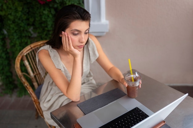 Mujer tomando un café helado mientras usa una computadora portátil