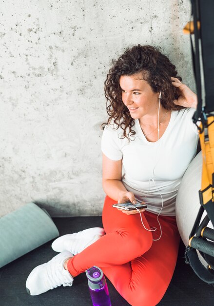 Mujer tomando un descanso después del entrenamiento y escuchando música en el teléfono celular en el gimnasio