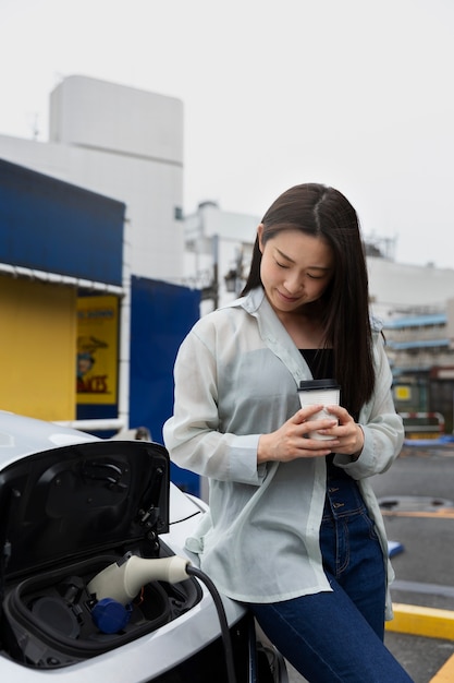 Mujer tomando un descanso para tomar café mientras su auto eléctrico se está cargando