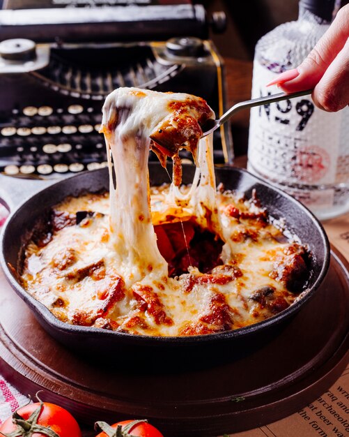 Mujer tomando estofado de carne con queso de una sartén negra con cubiertos.