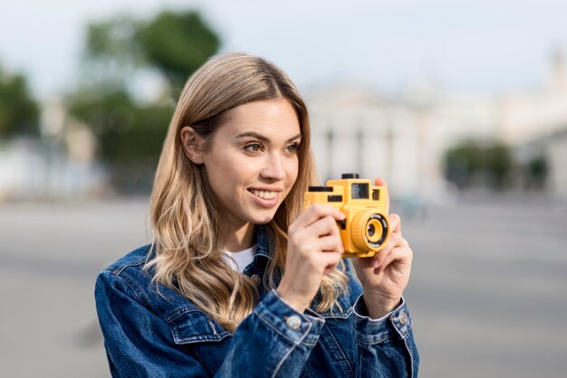Mujer tomando una foto con cámara amarilla fondo borroso