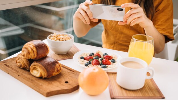 Mujer tomando foto de desayuno en mesa blanca