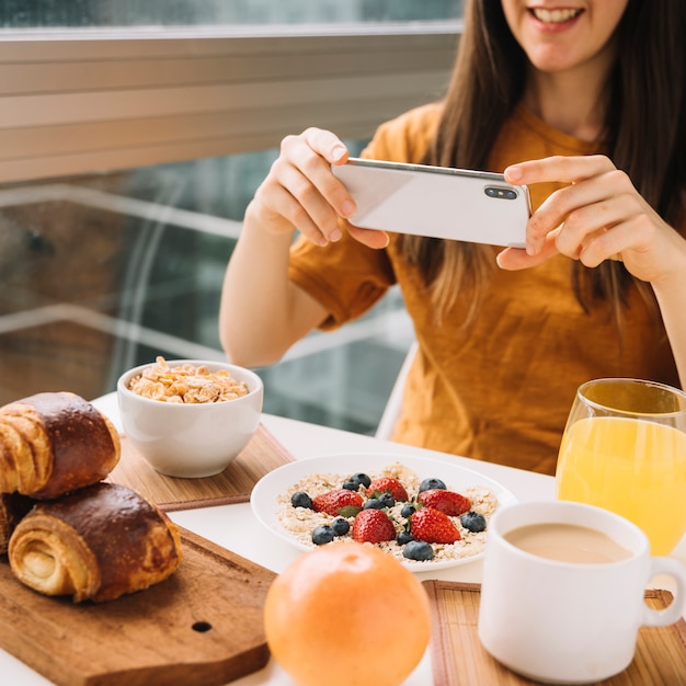 Mujer tomando foto de desayuno en mesa