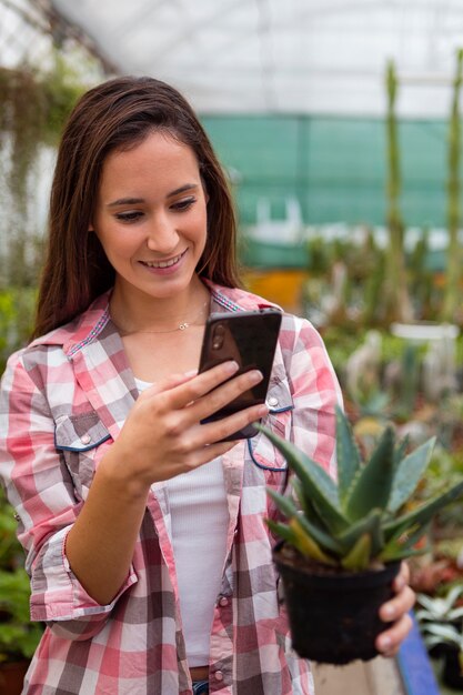 Mujer tomando foto de planta con teléfono en invernadero