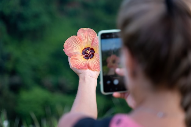 Mujer tomando una foto con su teléfono móvil de una flor que está sosteniendo en su mano