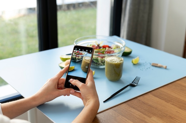 Mujer tomando una foto de un tazón con ensalada y un batido