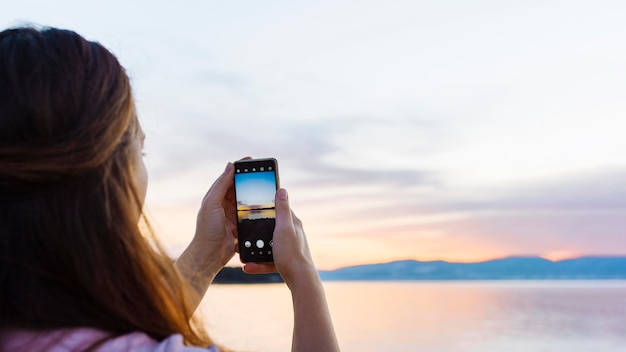 Mujer tomando una foto con el teléfono inteligente de la puesta del sol