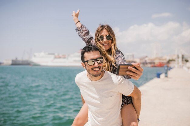 Mujer tomando una fotografía de su novio disfrutando de un paseo a cuestas en la espalda