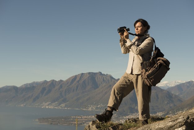 Mujer tomando fotografías desde una montaña con vistas a un lago en Ticino, Suiza