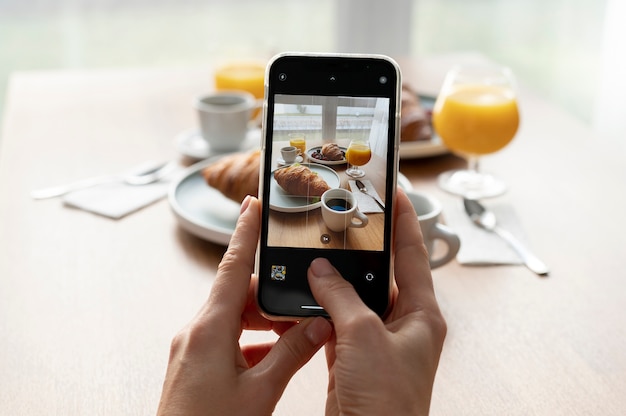 Mujer tomando fotos de dos croissants y dos vasos de jugo de naranja