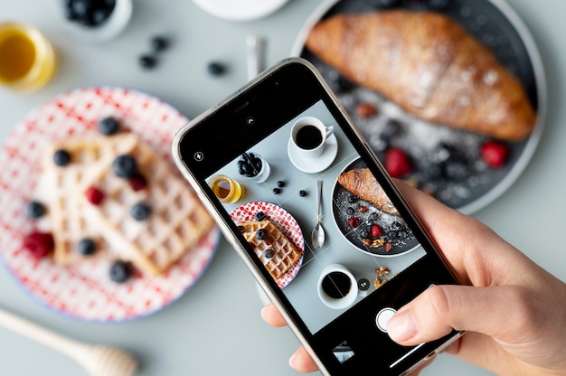 Mujer tomando fotos de gofres y un croissant con frutas