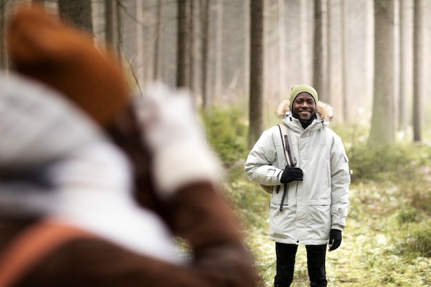 Foto gratuita mujer tomando fotos del hombre en el bosque durante un viaje por carretera de invierno