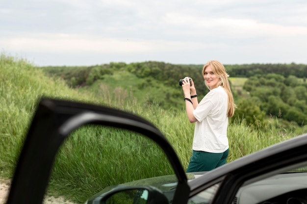 Mujer tomando fotos de la naturaleza delante del coche