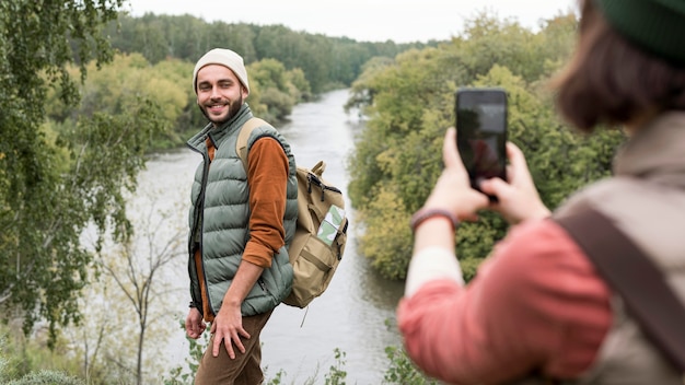 Mujer tomando fotos de novio en la naturaleza con smartphone