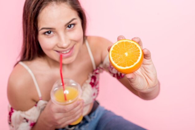 Mujer tomando jugo y sosteniendo rodajas de naranja